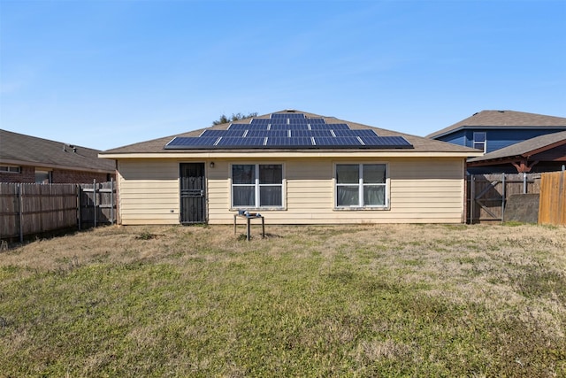 back of property with roof mounted solar panels, a fenced backyard, and a yard