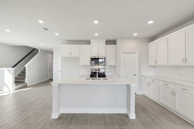 kitchen with light countertops, stainless steel microwave, gas stove, white cabinets, and light wood-type flooring