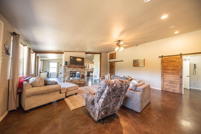 living room featuring a textured ceiling, ceiling fan, a barn door, a fireplace, and baseboards