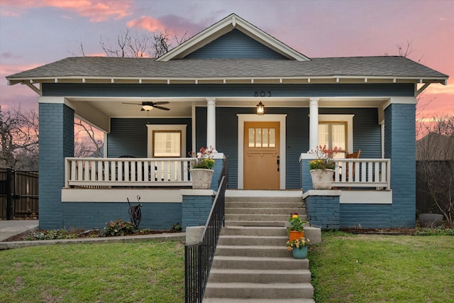 bungalow-style home featuring covered porch, roof with shingles, a front yard, and brick siding