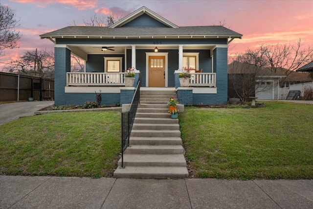 view of front of house featuring a porch, fence, a front lawn, and brick siding