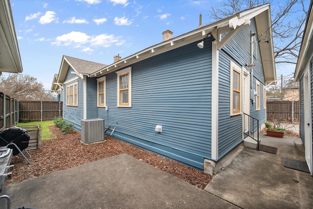 view of side of property with a patio, a chimney, cooling unit, and a fenced backyard