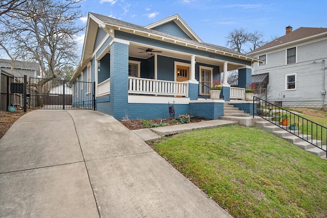 view of front of property with ceiling fan, a porch, brick siding, a gate, and a front yard