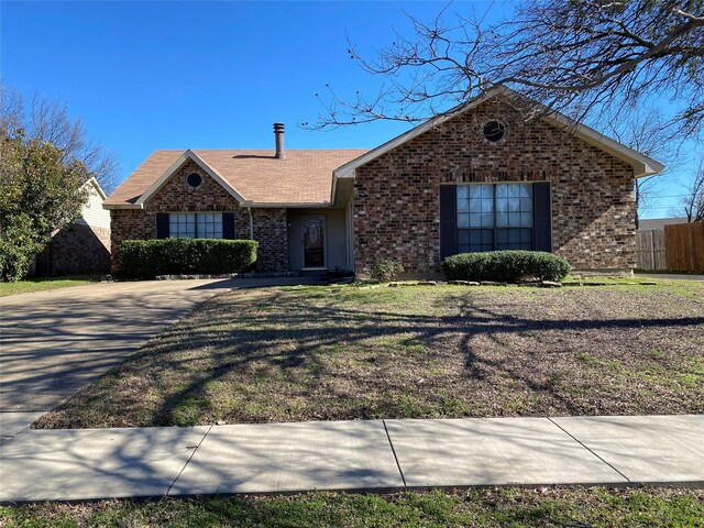 single story home featuring brick siding, fence, and a front lawn