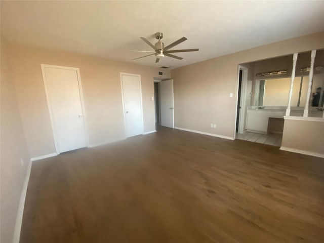 unfurnished bedroom featuring ceiling fan, ensuite bathroom, baseboards, and wood finished floors