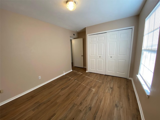unfurnished bedroom with wood finished floors, baseboards, and a closet