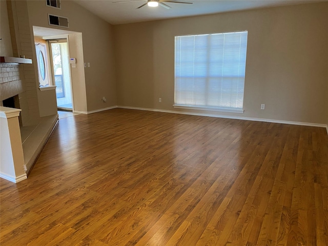 empty room featuring visible vents, wood finished floors, ceiling fan, and a fireplace
