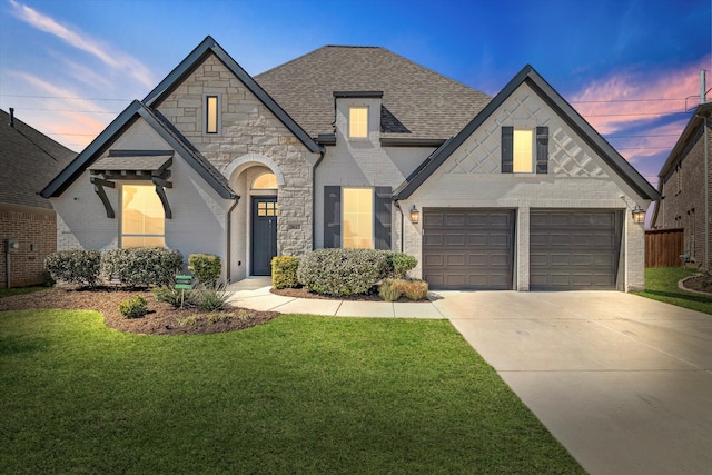 french country home featuring brick siding, roof with shingles, concrete driveway, and a front lawn