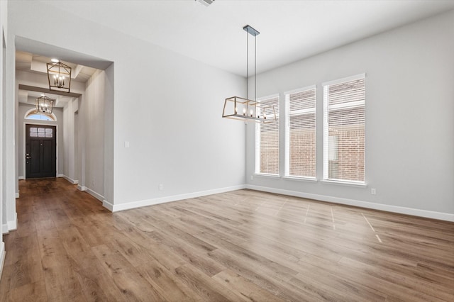 unfurnished dining area featuring a wealth of natural light, baseboards, an inviting chandelier, and light wood-style flooring