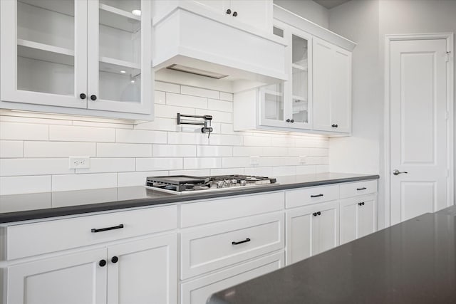 kitchen featuring custom range hood, dark countertops, white cabinetry, decorative backsplash, and stainless steel gas cooktop