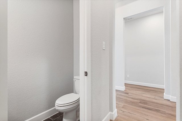 bathroom featuring a textured wall, toilet, baseboards, and wood finished floors