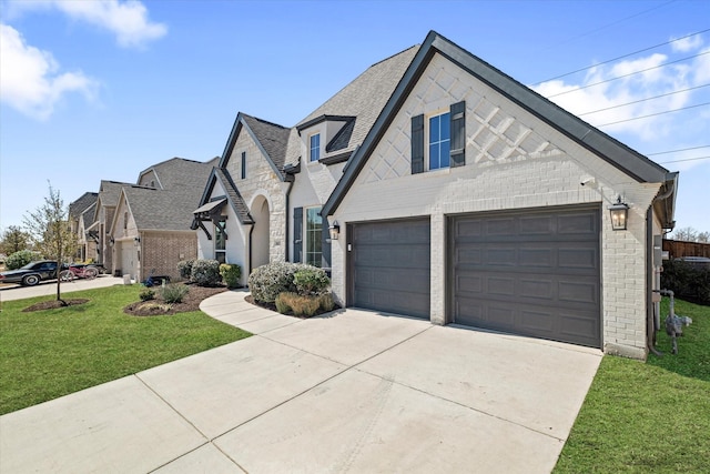 french country style house with a front lawn, brick siding, driveway, and a shingled roof