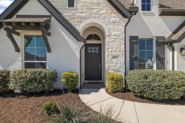 doorway to property with stone siding, brick siding, and a shingled roof