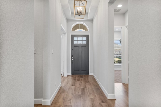 entryway featuring wood finished floors, visible vents, baseboards, a textured wall, and a chandelier