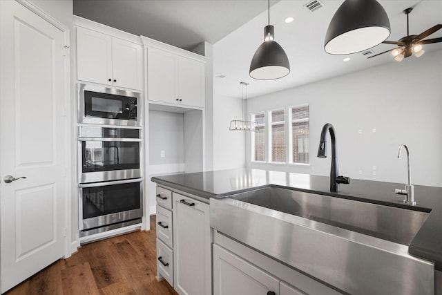 kitchen with dark wood finished floors, built in microwave, a sink, pendant lighting, and dark countertops