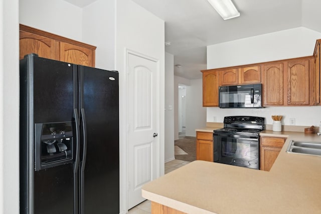 kitchen featuring light countertops, brown cabinetry, light tile patterned flooring, a sink, and black appliances