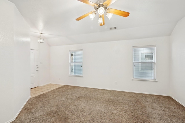 carpeted spare room with visible vents, a ceiling fan, vaulted ceiling, tile patterned flooring, and baseboards