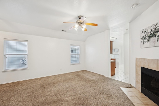 unfurnished living room featuring a tiled fireplace, light colored carpet, ceiling fan, vaulted ceiling, and light tile patterned flooring