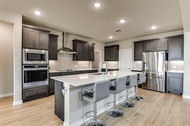 kitchen with stainless steel appliances, visible vents, light wood-style floors, a sink, and wall chimney range hood