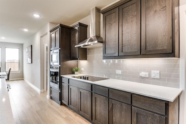 kitchen with dark brown cabinetry, stainless steel appliances, light countertops, wall chimney range hood, and tasteful backsplash