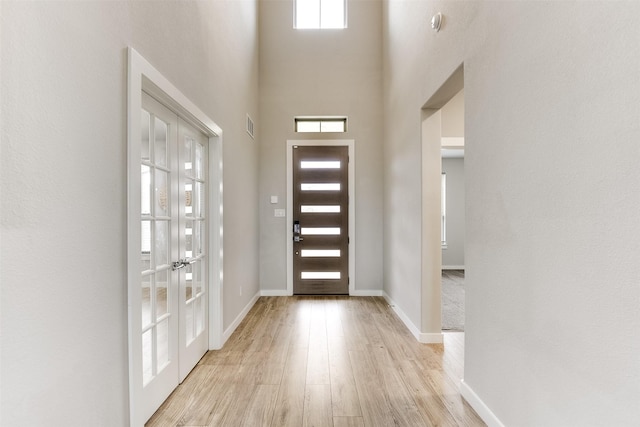 entrance foyer with baseboards, a high ceiling, visible vents, and light wood-style floors