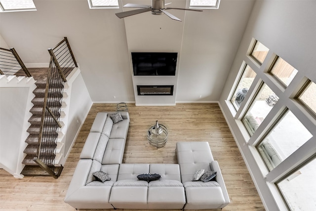 living room with a high ceiling, stairway, wood finished floors, and a glass covered fireplace