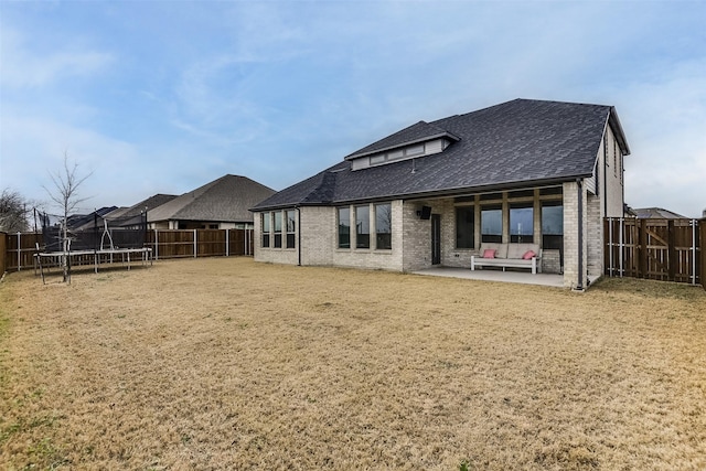 rear view of house featuring a patio, a fenced backyard, brick siding, a shingled roof, and a trampoline