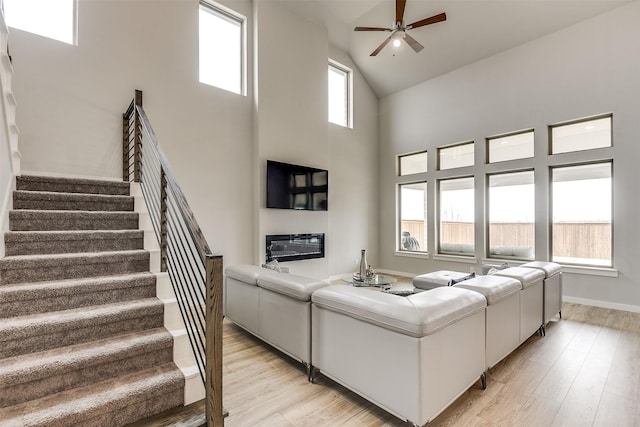 living room featuring high vaulted ceiling, stairway, light wood-style flooring, and a ceiling fan