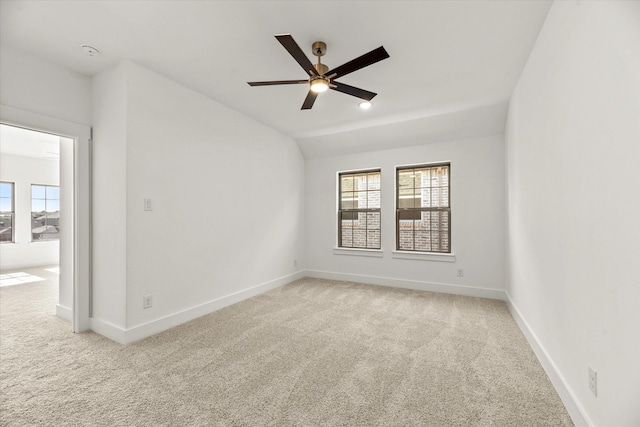 carpeted empty room featuring baseboards, vaulted ceiling, and a ceiling fan