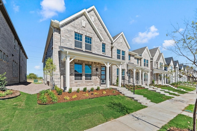 townhome / multi-family property featuring a porch, a residential view, brick siding, and a front lawn