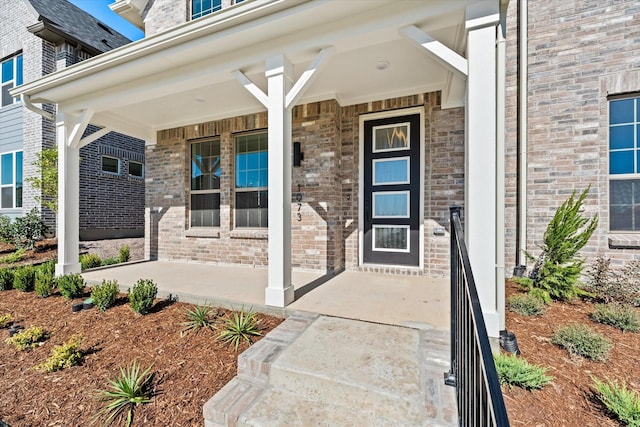 doorway to property featuring covered porch and brick siding