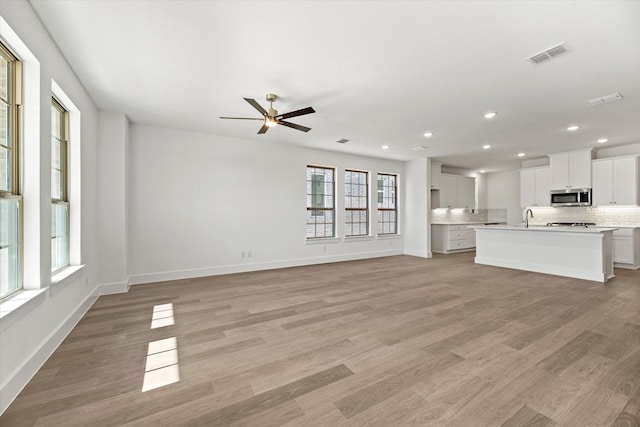 unfurnished living room with light wood finished floors, visible vents, a sink, and recessed lighting