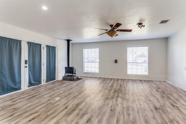 unfurnished living room with visible vents, light wood-style flooring, a ceiling fan, a wood stove, and baseboards