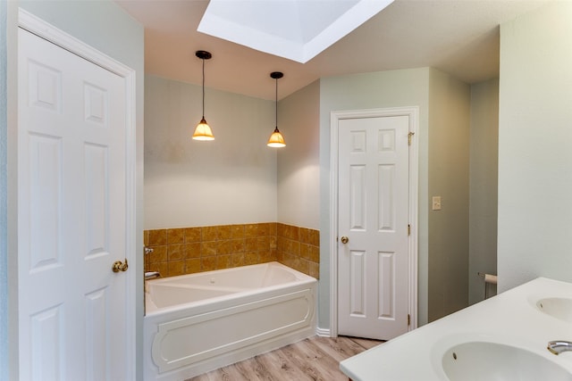 bathroom with a skylight, a garden tub, a sink, and wood finished floors