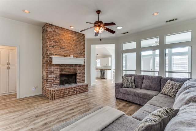 living room featuring ornamental molding, light wood-style floors, visible vents, and a fireplace