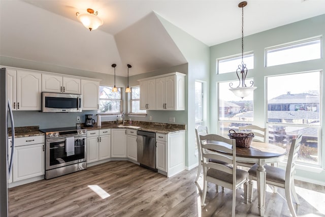 kitchen with decorative light fixtures, stainless steel appliances, white cabinets, vaulted ceiling, and light wood-type flooring