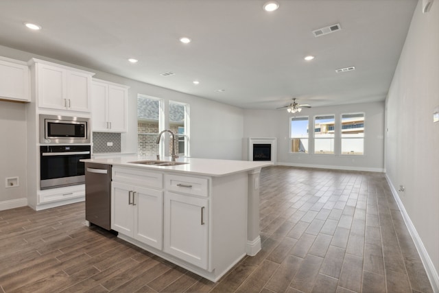 kitchen featuring stainless steel appliances, a fireplace, a sink, visible vents, and wood tiled floor