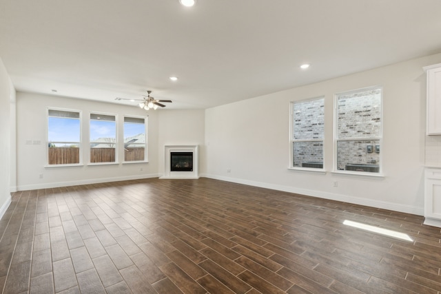unfurnished living room featuring a ceiling fan, dark wood-style floors, baseboards, recessed lighting, and a glass covered fireplace