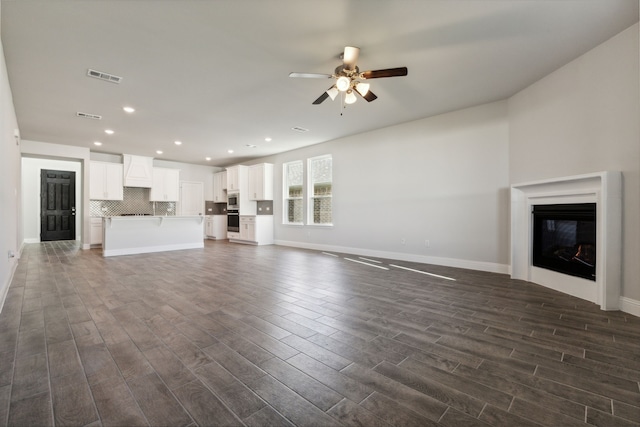 unfurnished living room with dark wood finished floors, a glass covered fireplace, visible vents, and a ceiling fan