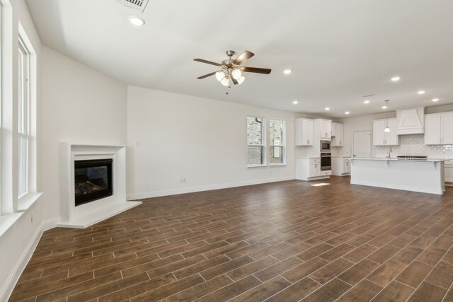 unfurnished living room with dark wood-style floors, a glass covered fireplace, recessed lighting, and a ceiling fan