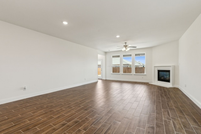 unfurnished living room with a glass covered fireplace, dark wood-style floors, baseboards, and ceiling fan