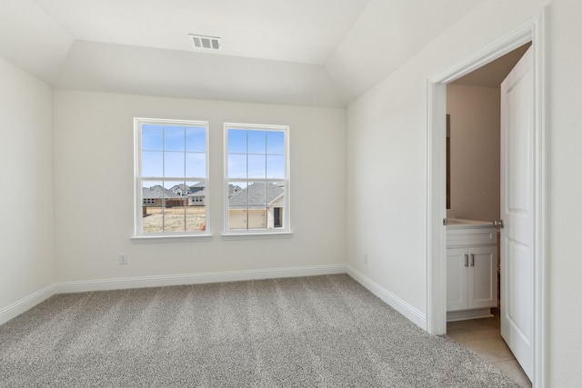 spare room featuring visible vents, baseboards, lofted ceiling, and light carpet