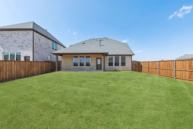 back of house with a yard, brick siding, a fenced backyard, and a shingled roof