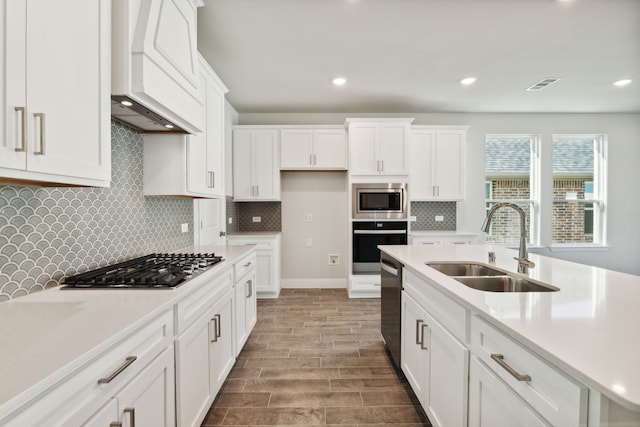 kitchen with stainless steel appliances, custom range hood, visible vents, white cabinetry, and a sink