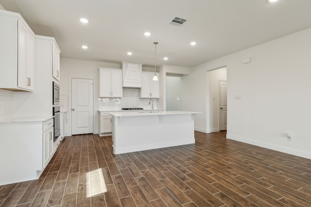 kitchen with visible vents, dark wood finished floors, a center island with sink, decorative backsplash, and custom exhaust hood
