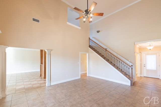 unfurnished living room featuring visible vents, a ceiling fan, a towering ceiling, stairs, and ornate columns