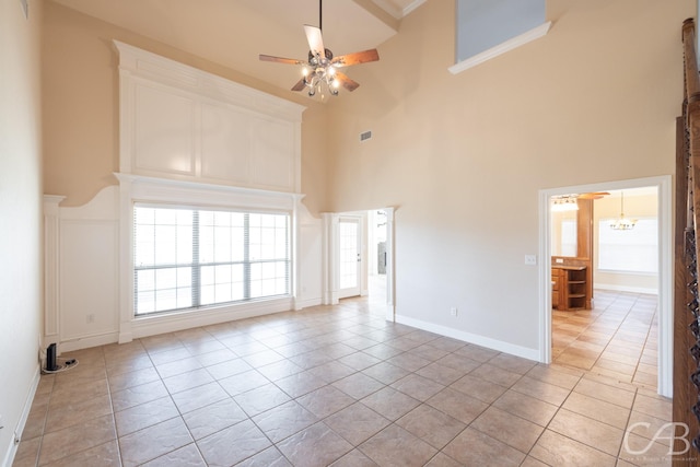 spare room with light tile patterned floors, ceiling fan with notable chandelier, a towering ceiling, and baseboards