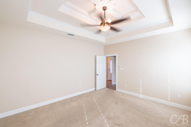 empty room featuring a raised ceiling, light colored carpet, visible vents, ornamental molding, and baseboards