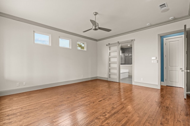 unfurnished bedroom with a barn door, wood finished floors, visible vents, and crown molding