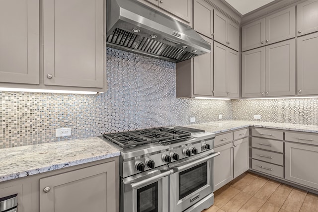 kitchen featuring backsplash, gray cabinetry, light stone countertops, double oven range, and under cabinet range hood